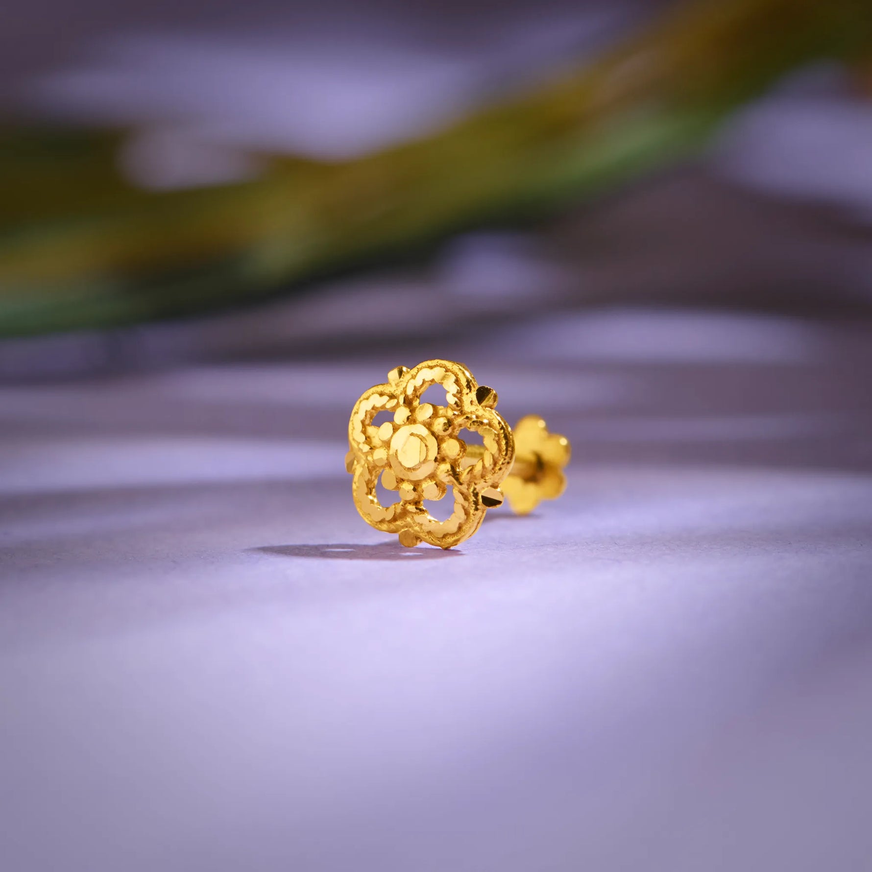 Close up of an intricate floral gold nose pin placed on a soft lavender surface highlighting detailed craftsmanship