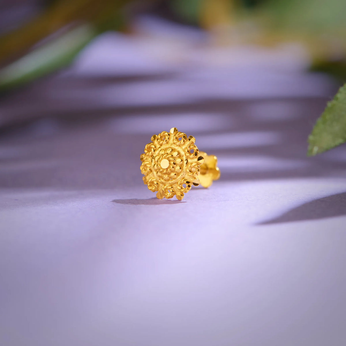 Close up of an ornate floral gold nose pin placed on a soft lavender background highlighting intricate handcrafted detailing