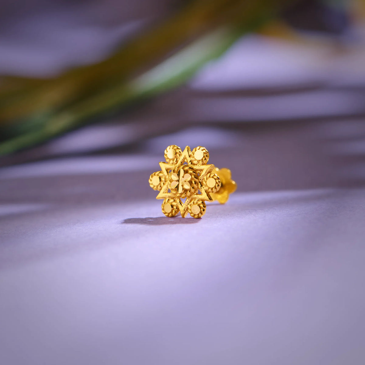 Floral cluster 18K nose pin gold placed on a soft lavender surface highlighting its detailed craftsmanship