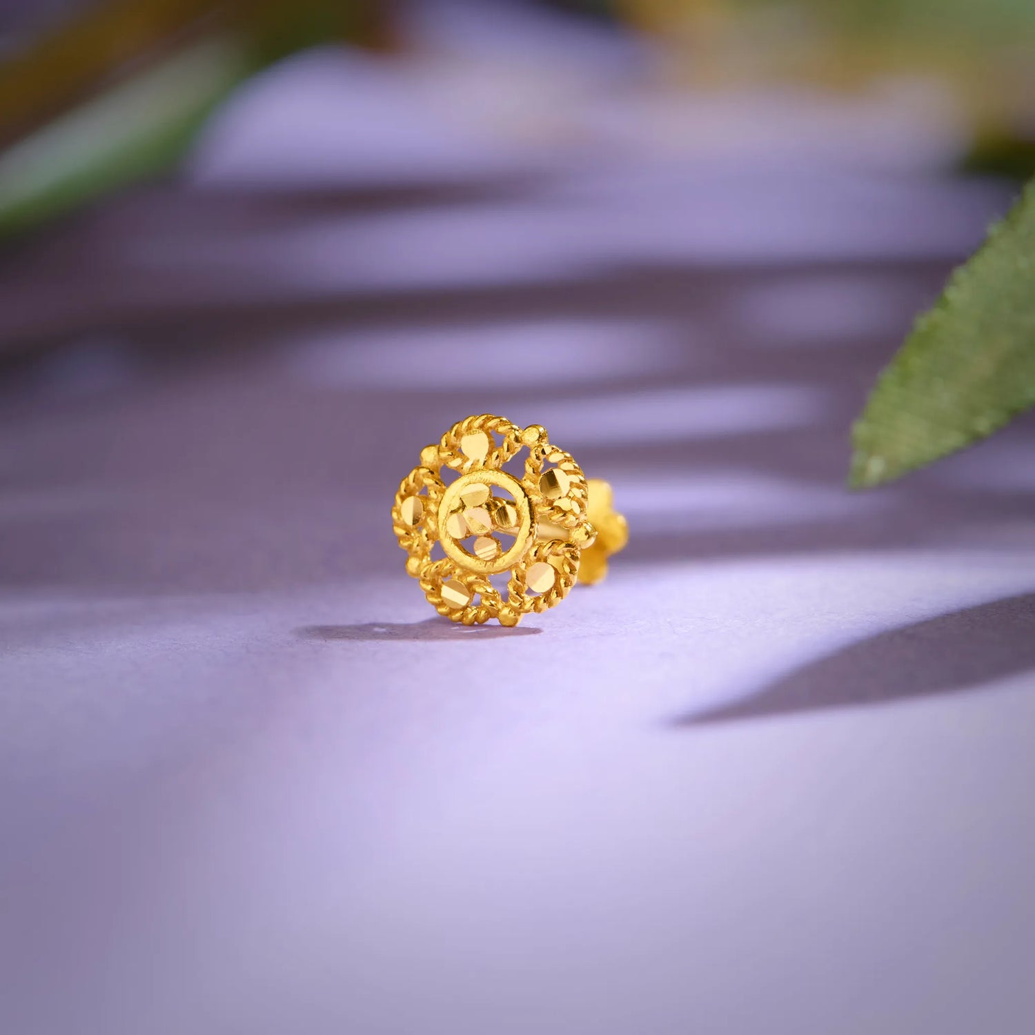 Close up of an intricate floral gold nose pin placed on a soft lavender surface highlighting detailed craftsmanship