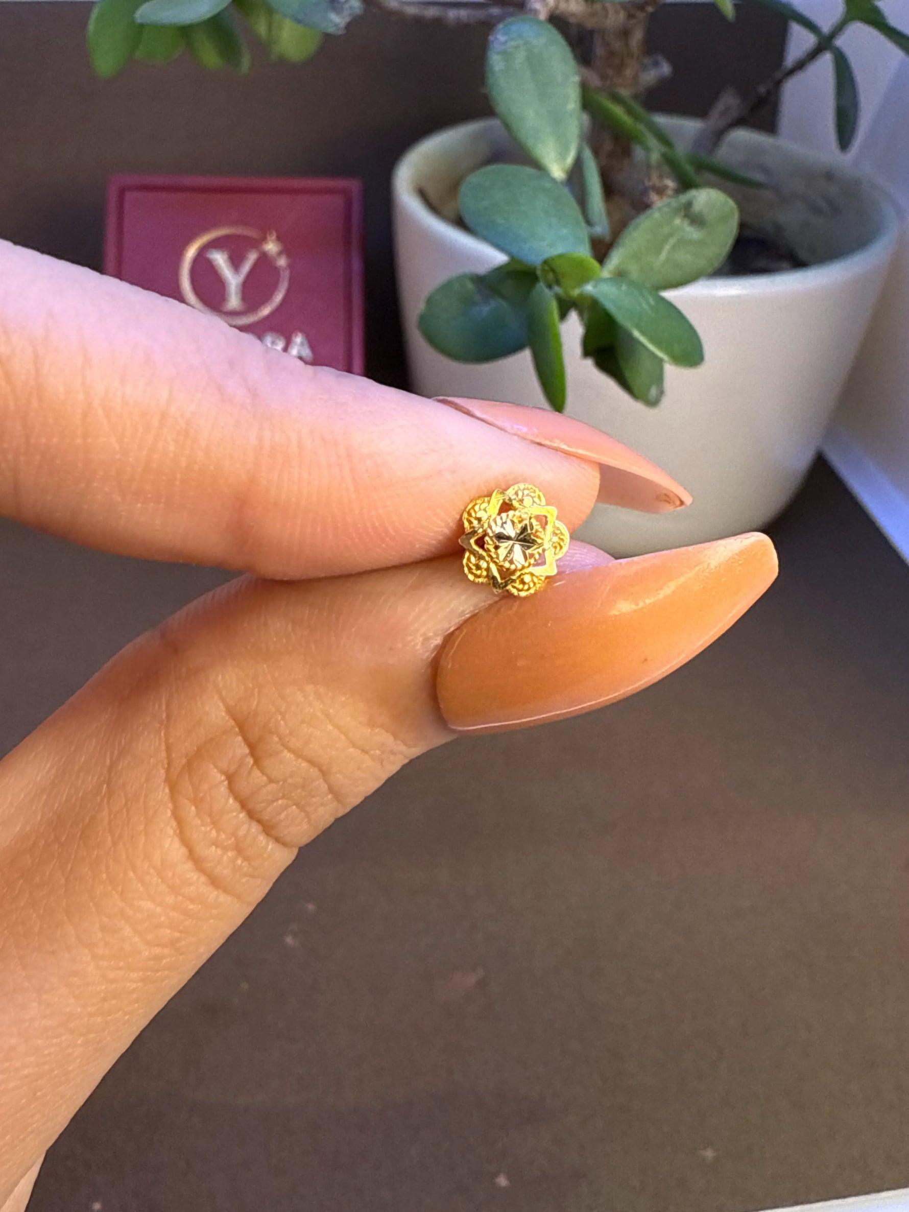 Hand holding a small floral gold nose pin near a plant to show size and real life proportion

