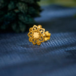 Close-up of floral patterned 18K nose pin gold placed on a textured blue surface highlighting its intricate detailing