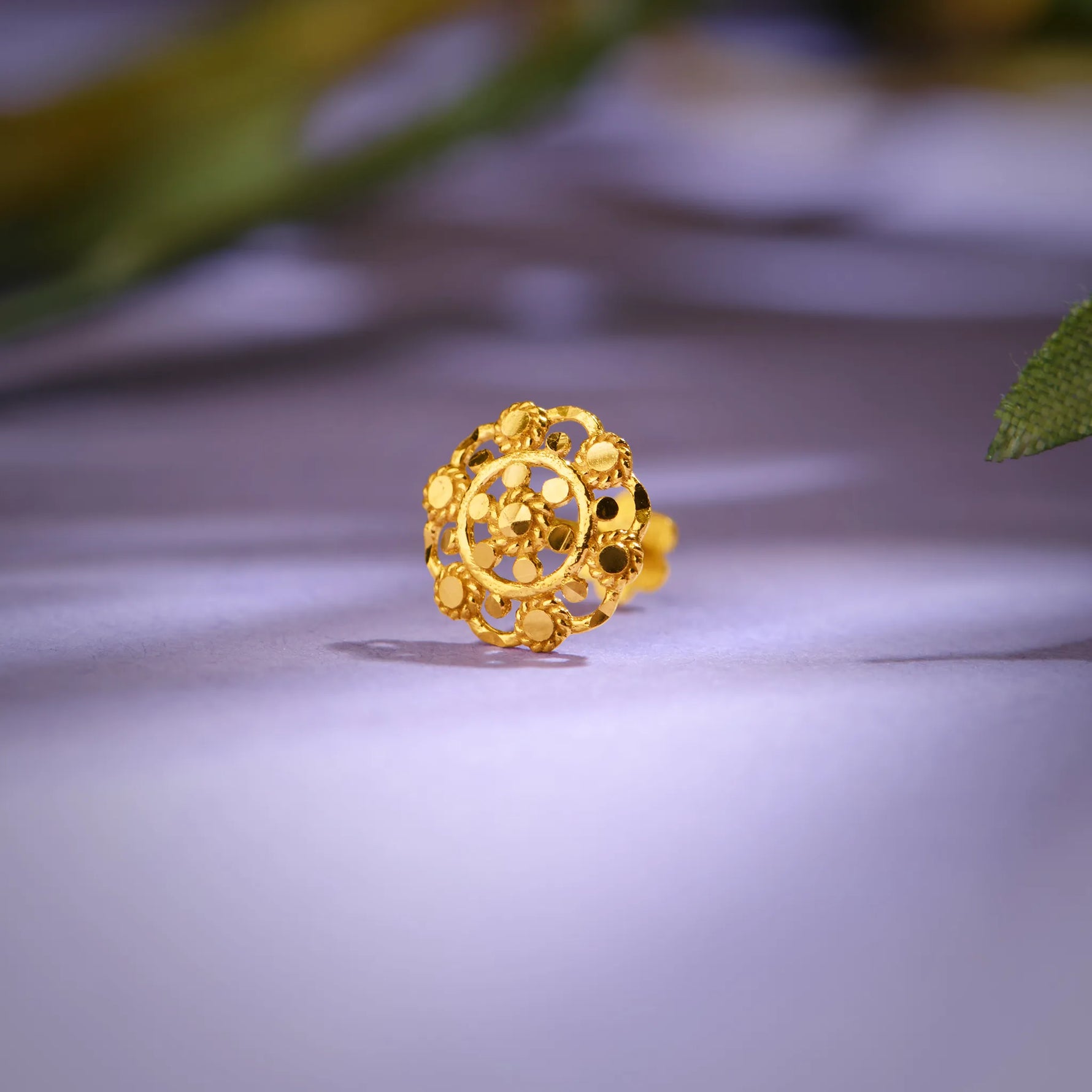 Close up of floral gold nose pin placed on a soft lavender background highlighting intricate cutwork design