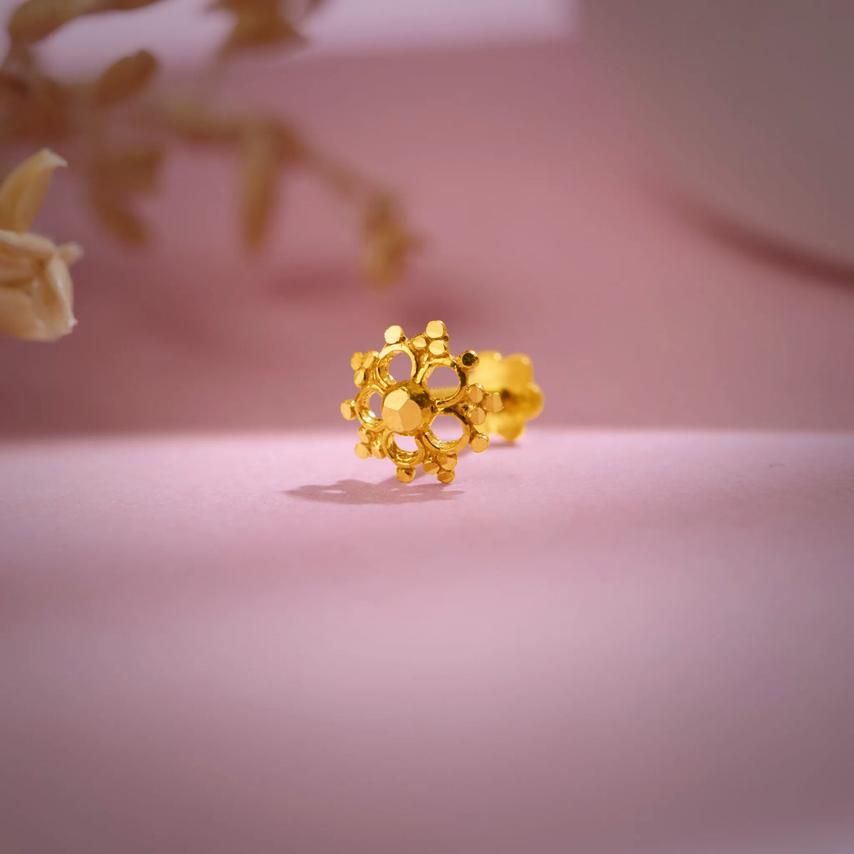 Floral cluster 18K nose pin gold placed on a soft pink background highlighting its intricate handcrafted detailing