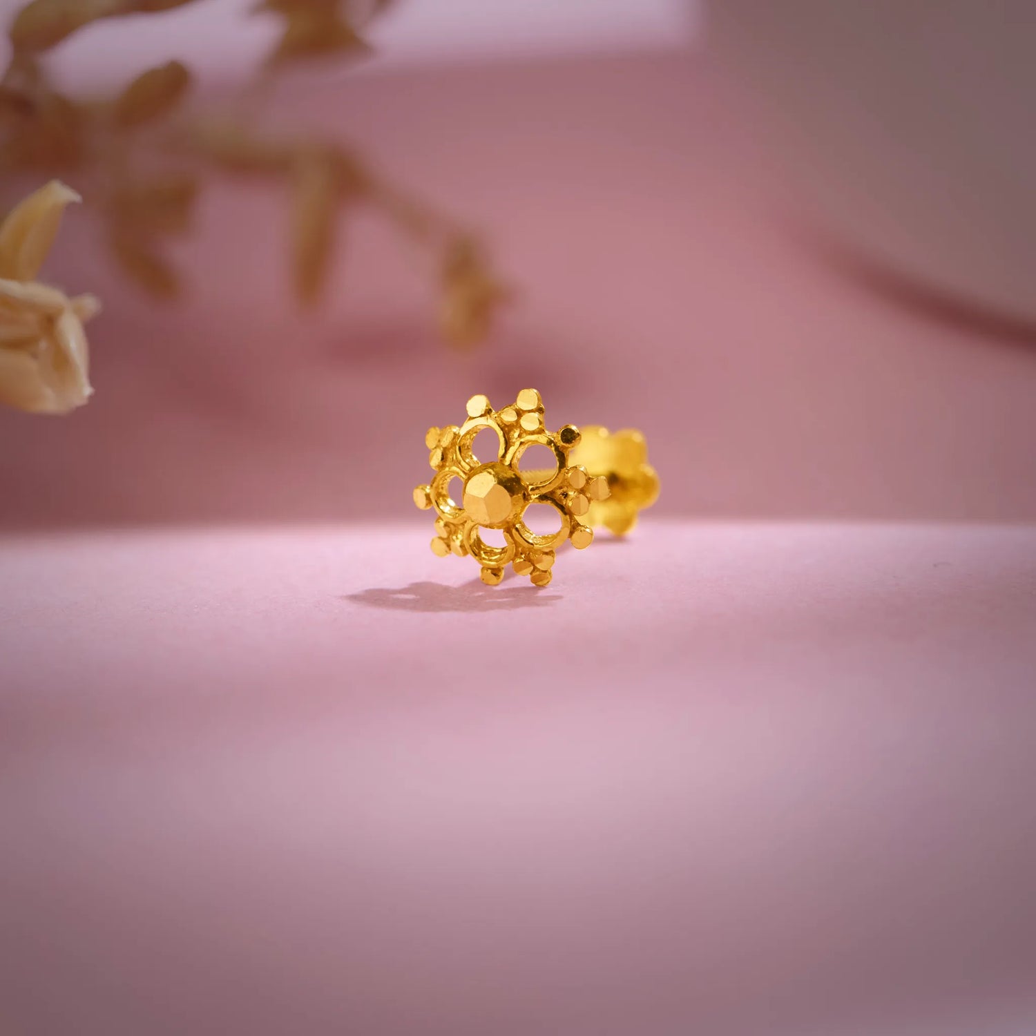 Floral cluster 18K nose pin gold placed on a soft pink background highlighting its intricate handcrafted detailing