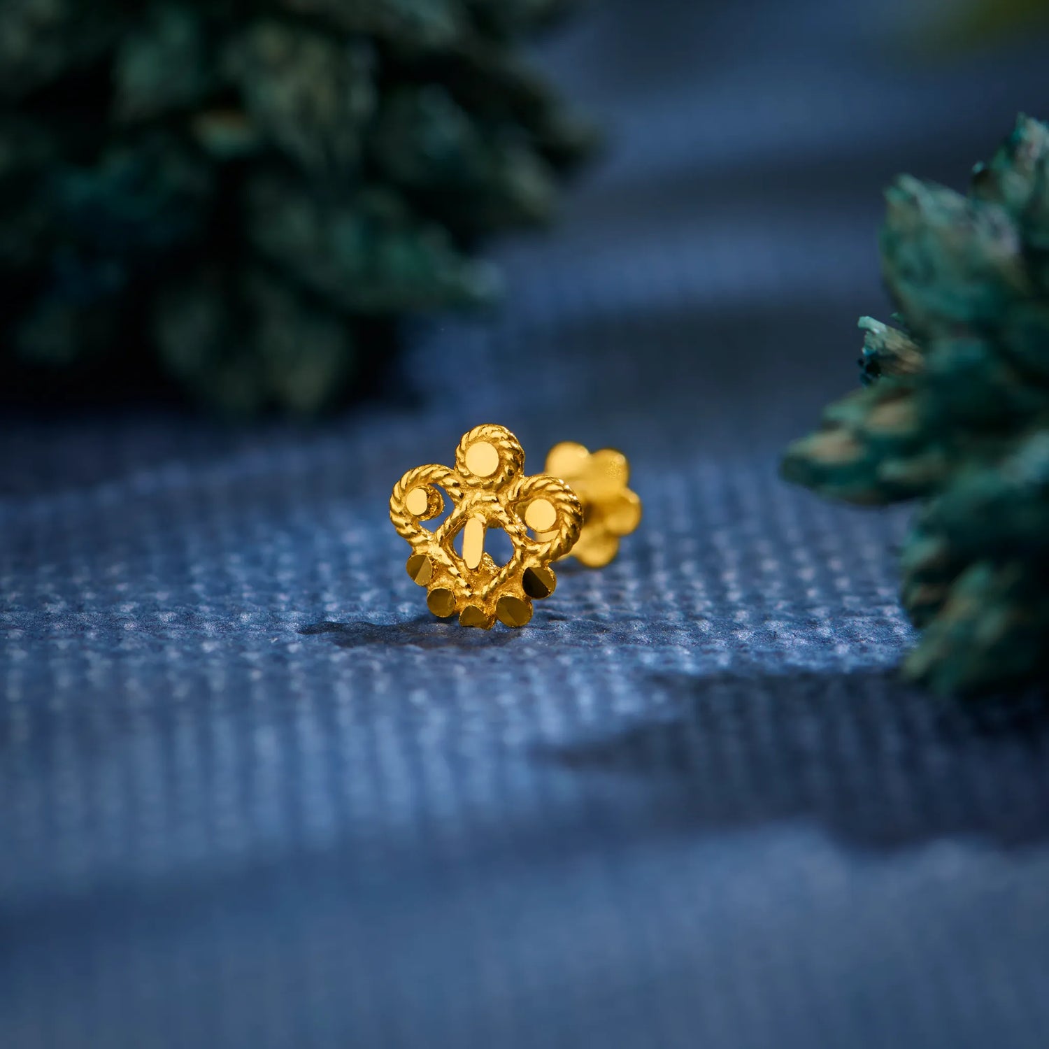 Close-up of floral 18K nose pin gold placed on a textured blue surface highlighting its intricate detailing