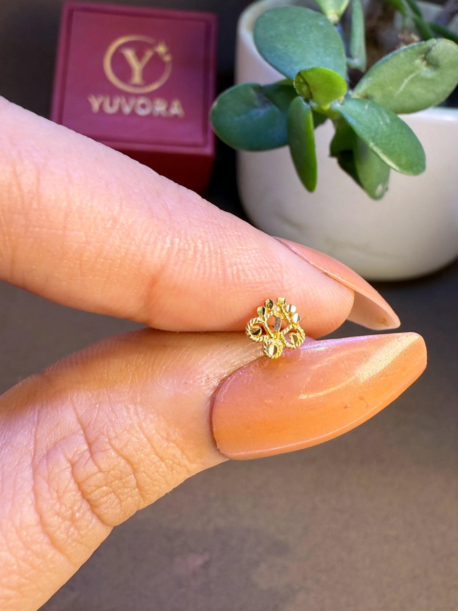Hand holding tiny floral 18K nose pin gold to show its small size and delicate craftsmanship
