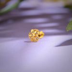 Close up of floral 18K gold nose pin placed on a soft lavender surface highlighting intricate openwork design