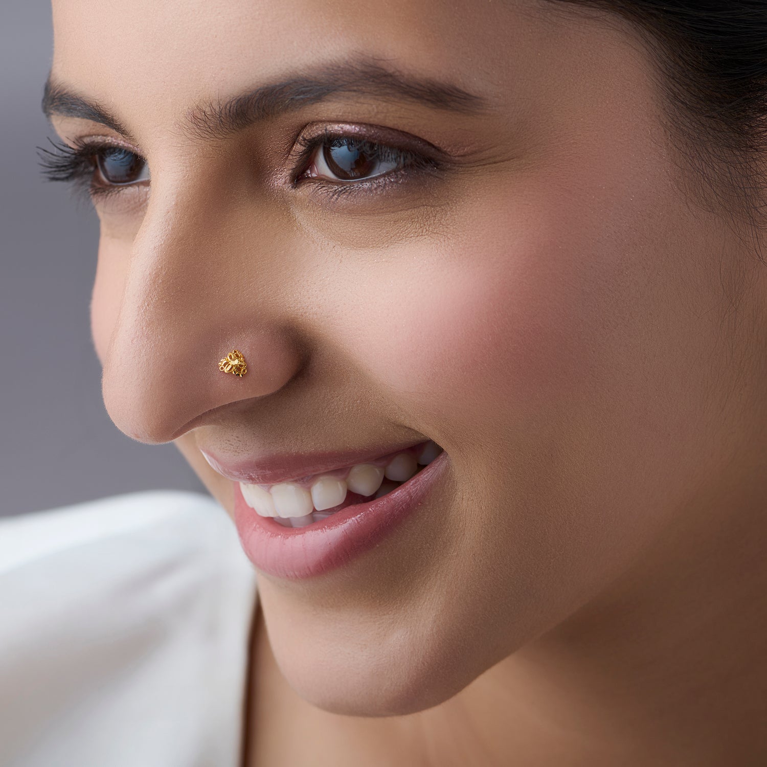 Woman wearing a small floral gold nose pin smiling softly showcasing a refined everyday jewellery look