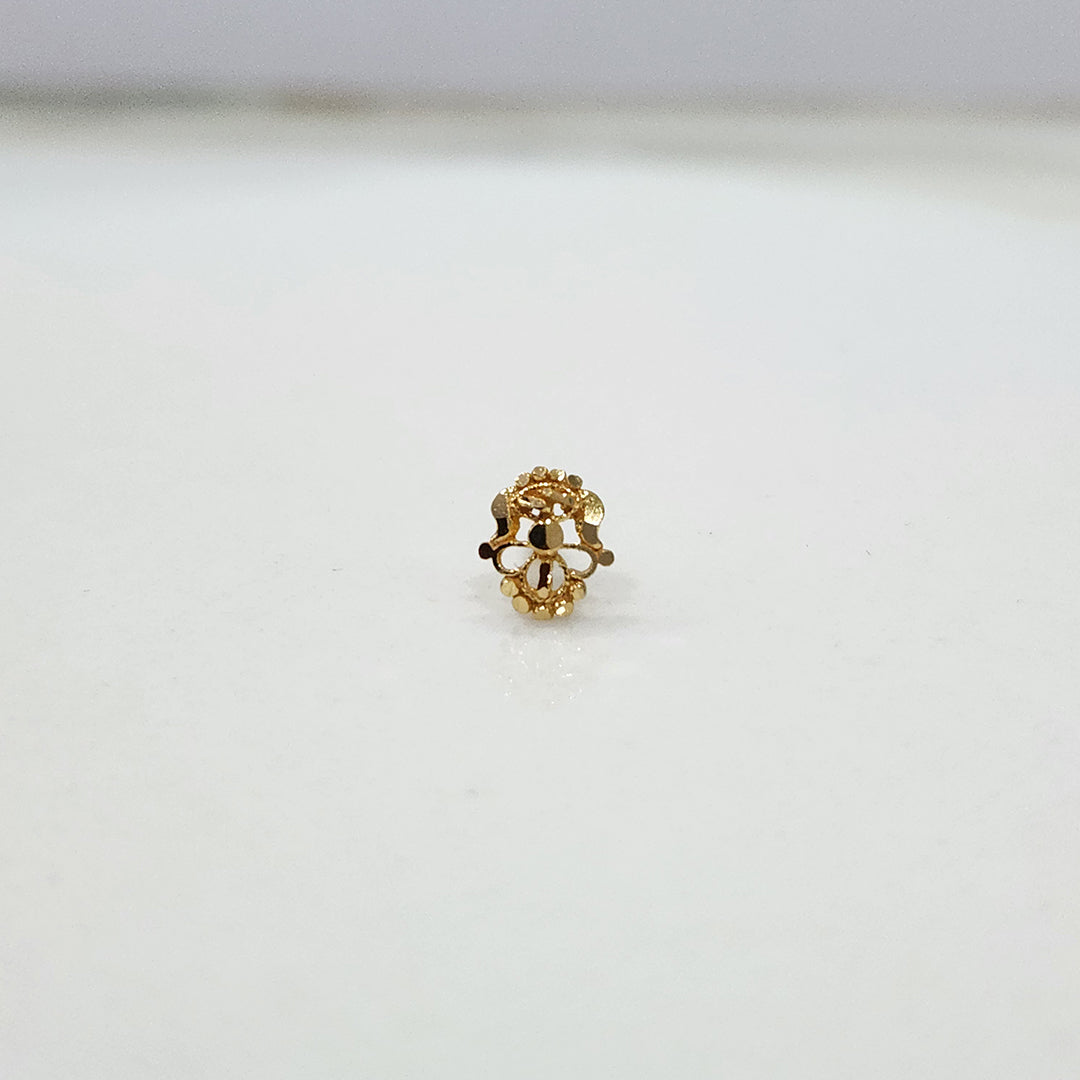Front view of a tiny gold nose pin placed on a white surface highlighting its compact floral design
