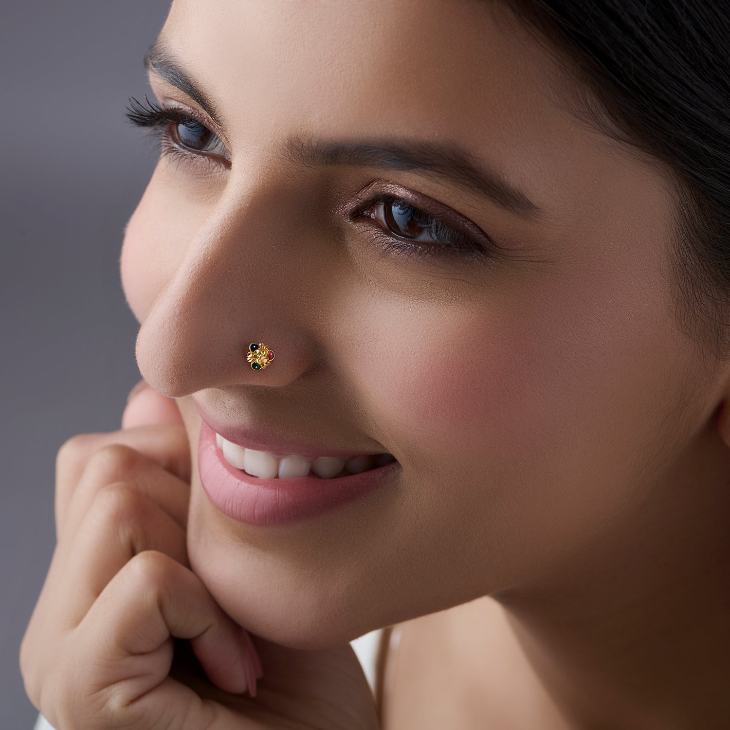 Woman wearing a small gold nose pin shown in a soft side profile with a pleasant smile