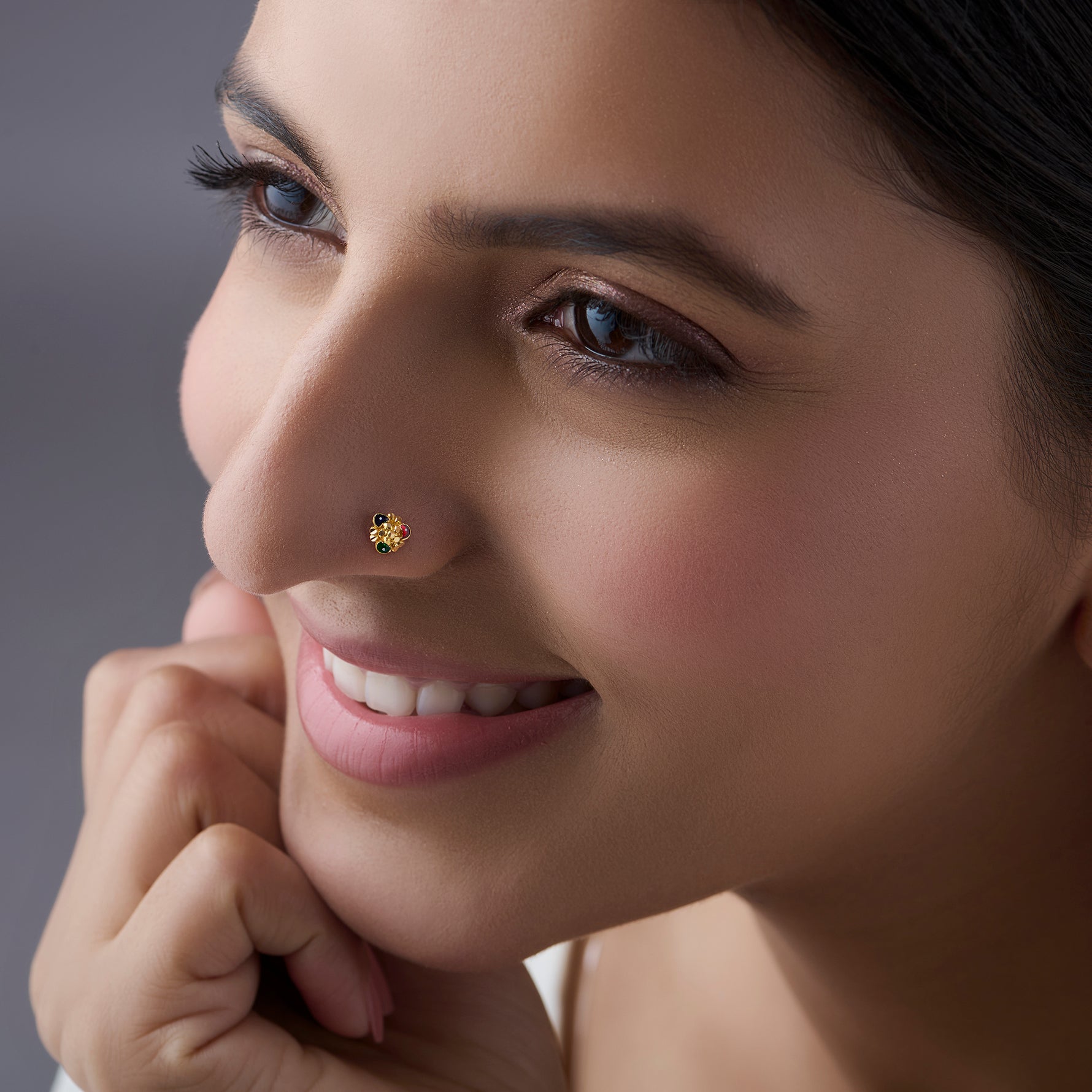 Woman wearing a small gold nose pin shown in a soft side profile with a pleasant smile