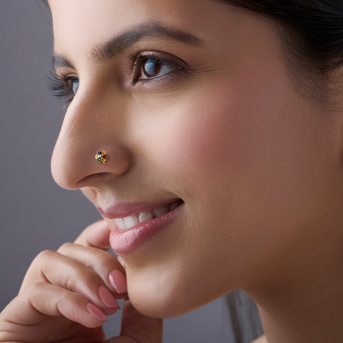 Woman wearing a small gold nose pin shown in a side profile with a gentle smile