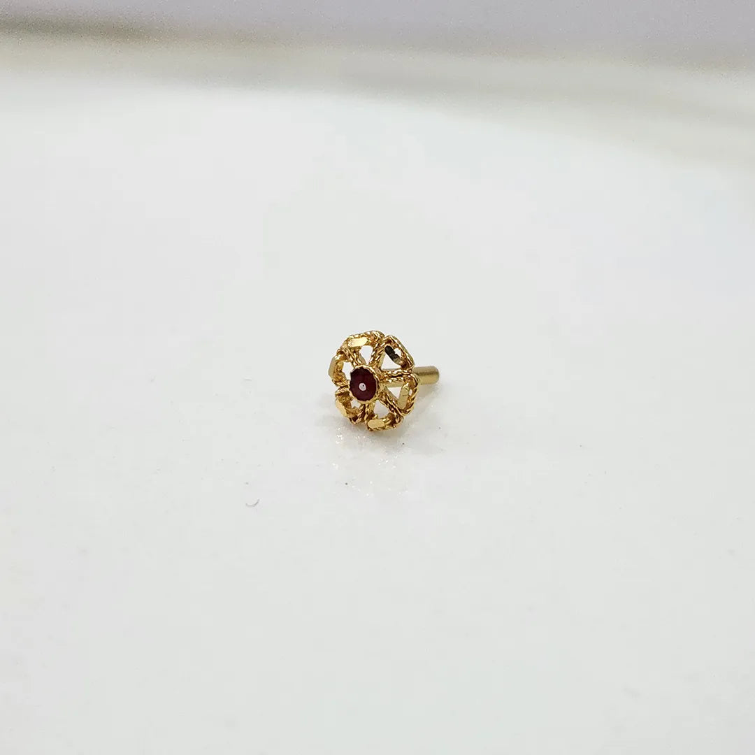 Close-up of tiny floral 18K nose pin gold on a clean white surface displaying its detailed carving
