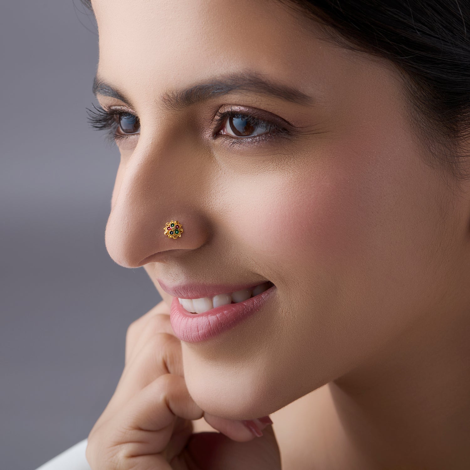 Woman wearing a small floral gold nose pin with green stones shown in a side profile