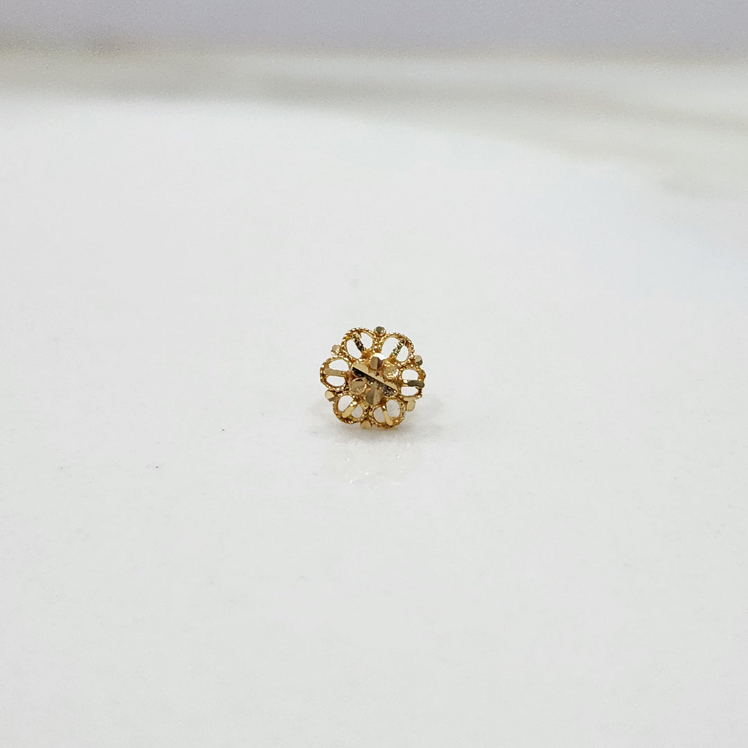 Close-up of small 18K nose pin gold on a marble surface showing its intricate flower-inspired design