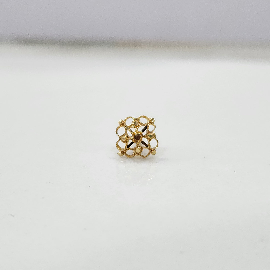 Close-up of small 18K nose pin gold showing its intricate geometric design on a clean surface