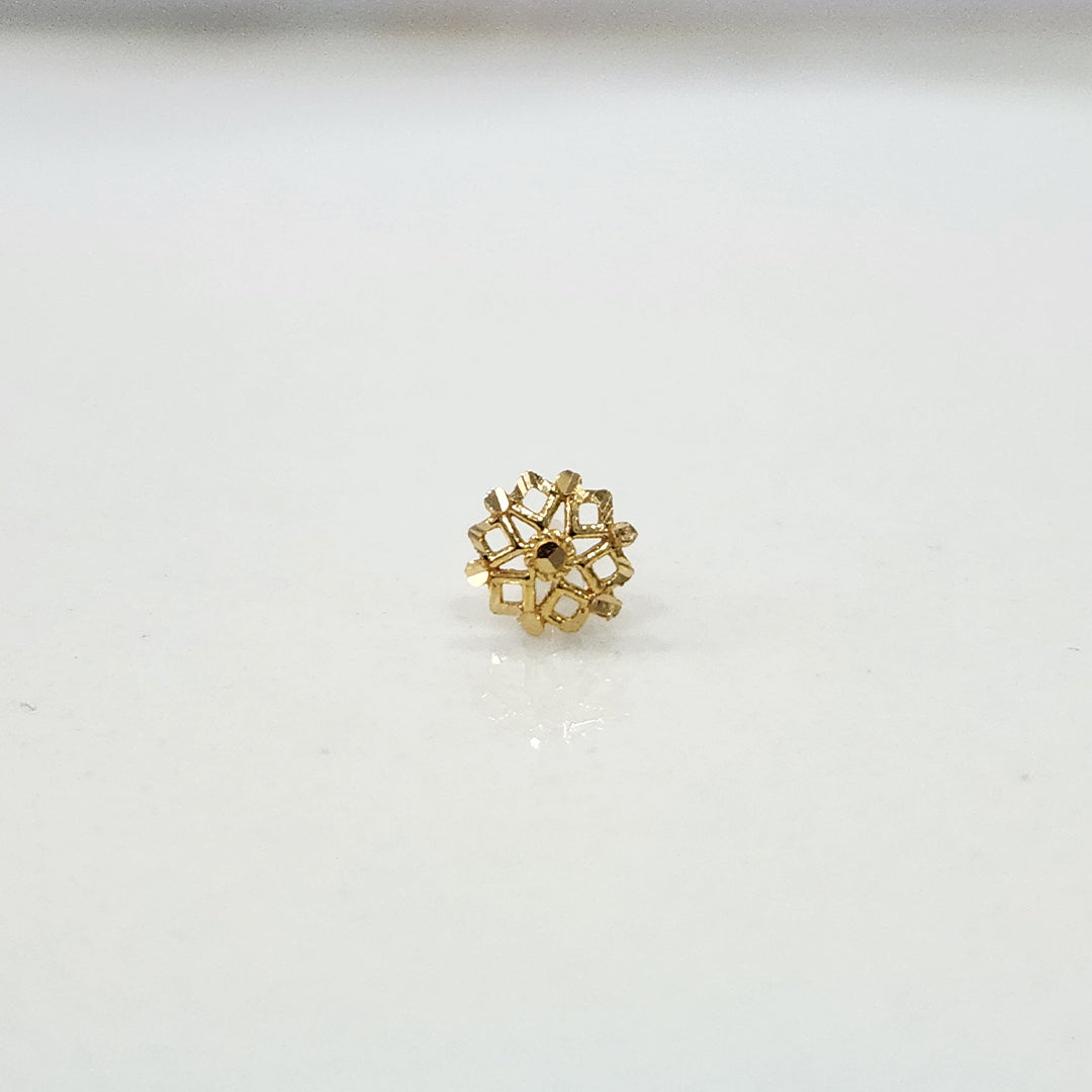 Slight angled view of floral gold nose pin on a white surface highlighting its delicate design