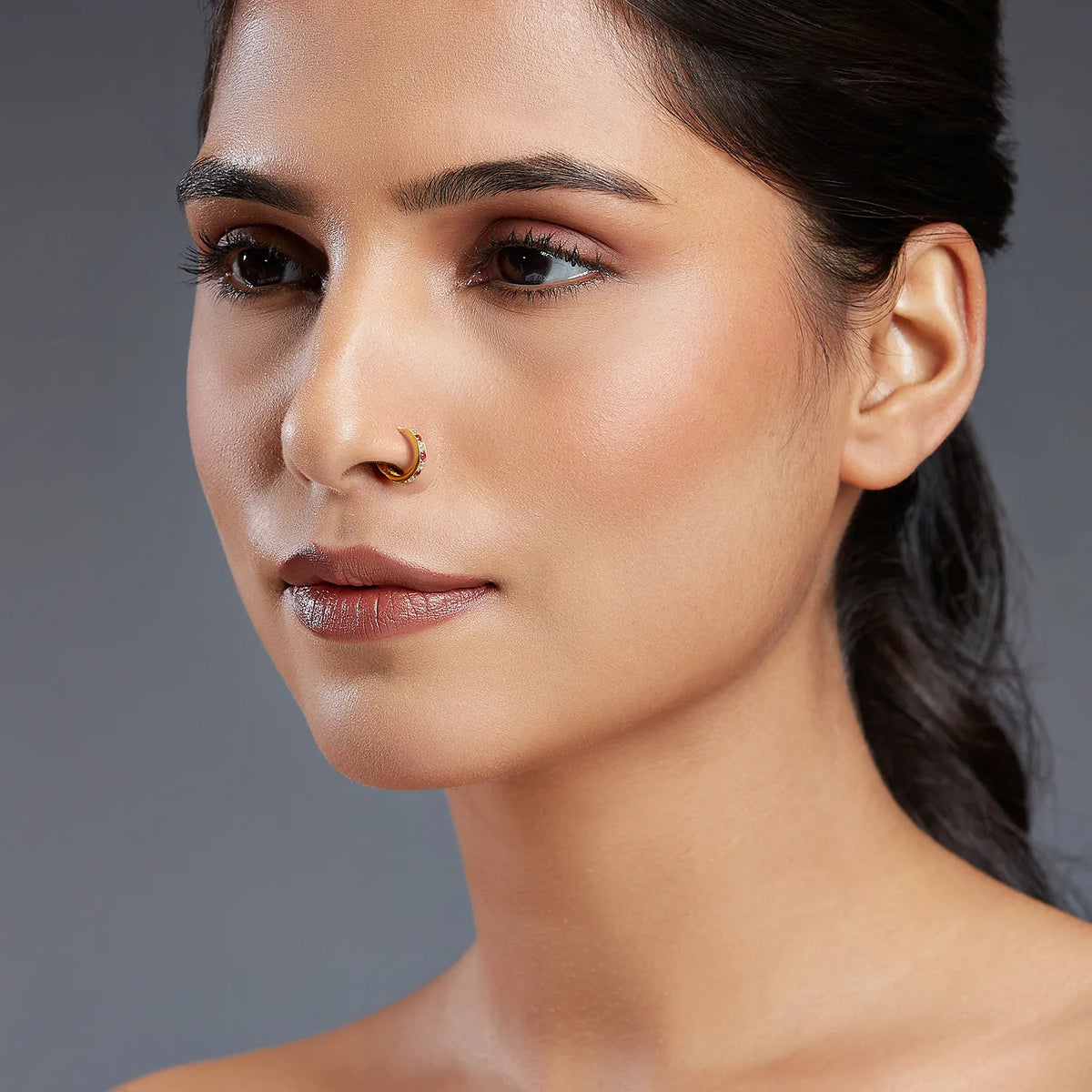 Front facing portrait of a woman wearing a slim gemstone gold nose ring for a clean modern look