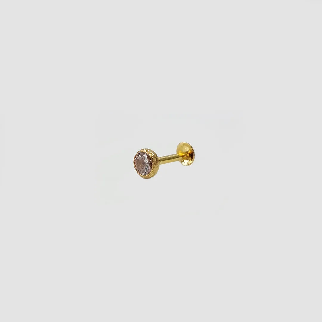 Gold stone nose pin with pink gemstone placed on light surface