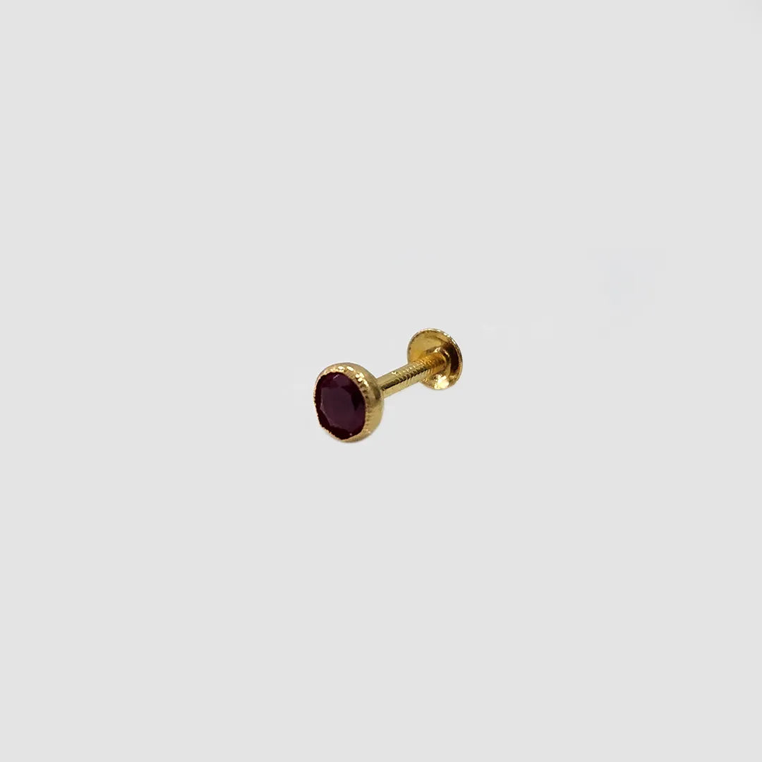 Gold stone nose pin with black gemstone placed on light surface