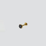 Close up of gold nose pin featuring black stone on light background