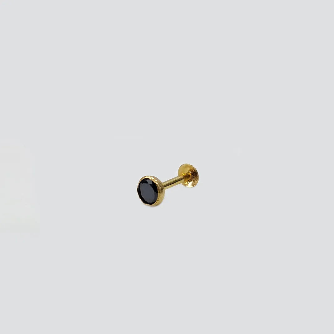 Close up of gold nose pin featuring black stone on light background