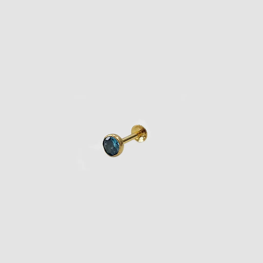 Gold nose pin with blue gemstone placed on light background
