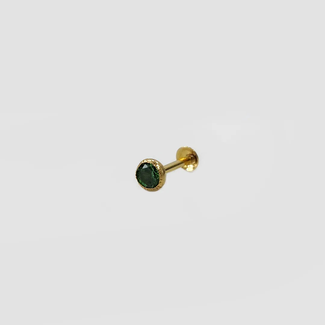 Side angle view of gold stone nose pin with green gemstone