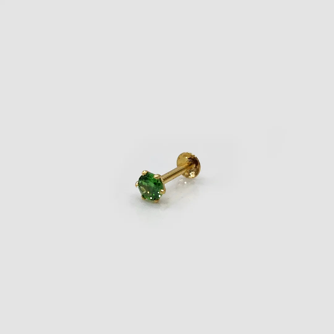 Close up of green stone gold nose pin placed upright on plain surface