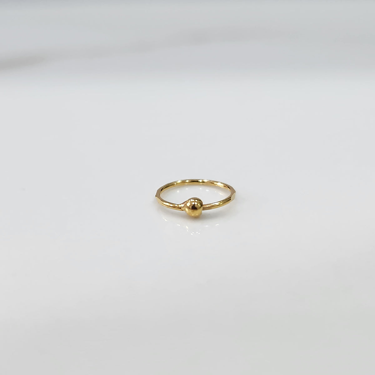 Close up of delicate open hoop gold nose ring placed flat on a white surface