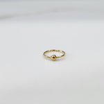 Close up of delicate open hoop gold nose ring placed flat on a white surface