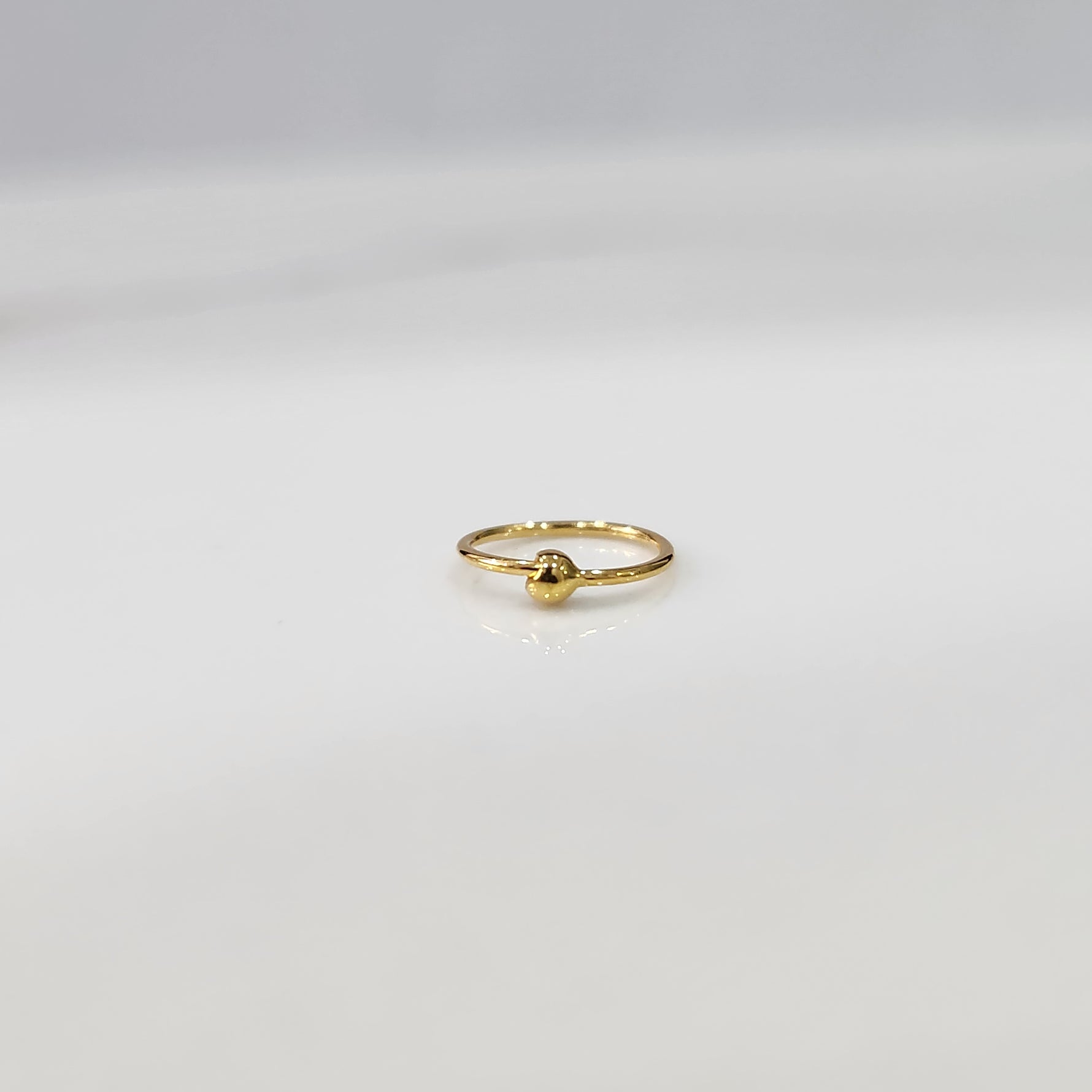 Close up of open hoop gold nose ring placed on a white background showing the clasp free open design
