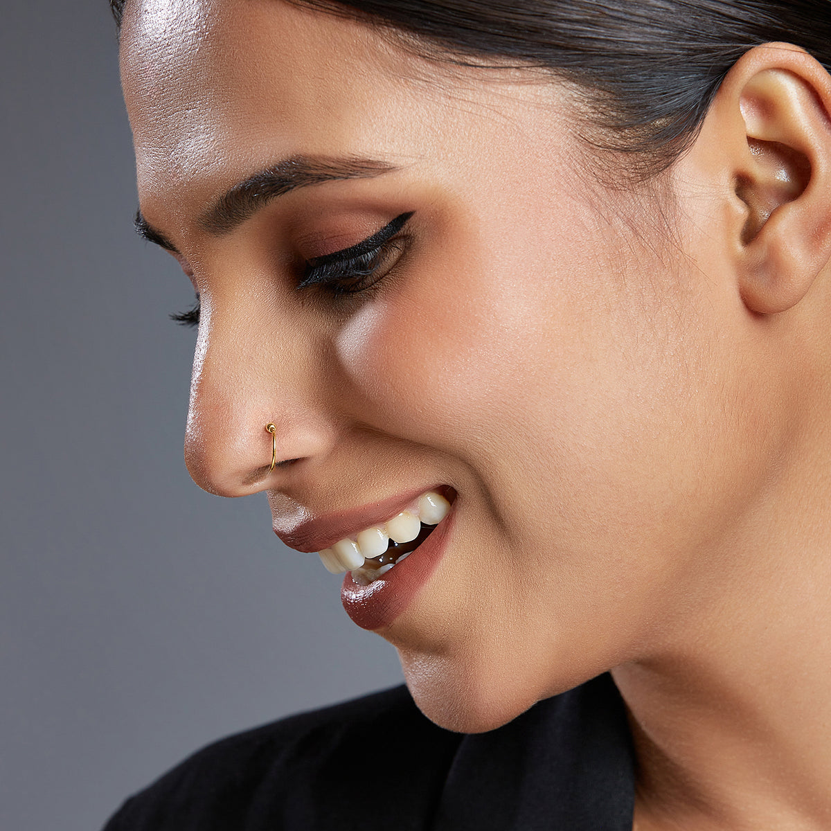 Woman smiling while wearing a simple gold nose ring captured in a soft profile view