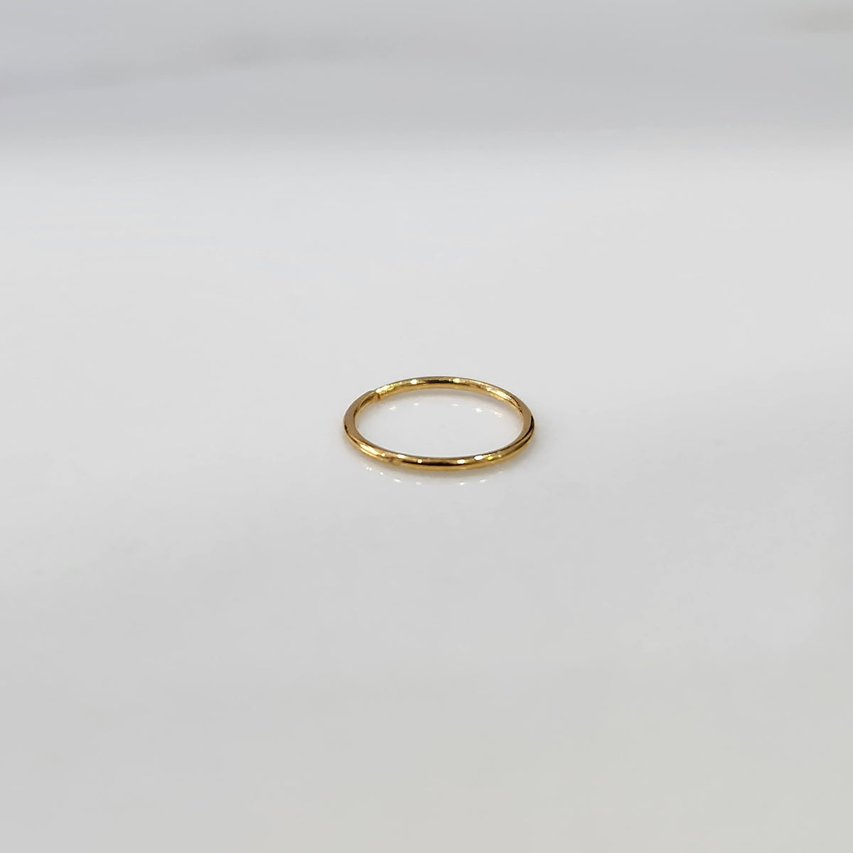 Top view of delicate plain gold hoop nose ring laid flat on a light grey surface