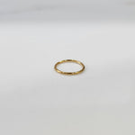 Top view of delicate plain gold hoop nose ring laid flat on a light grey surface