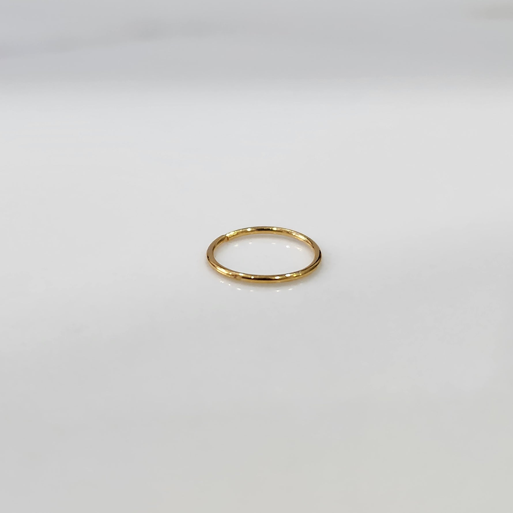 Top view of delicate plain gold hoop nose ring laid flat on a light grey surface
