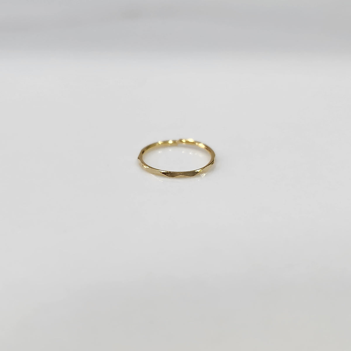 Flat lay view of a small plain gold hoop nose ring on a neutral surface showing true proportions