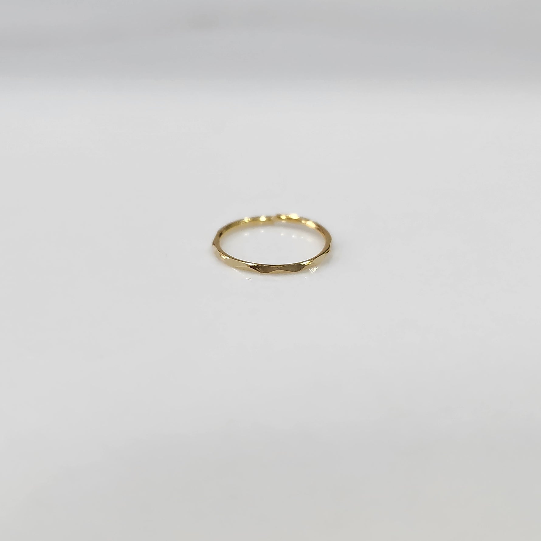 Flat lay view of a small plain gold hoop nose ring on a neutral surface showing true proportions