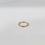 Flat lay view of small plain gold hoop nose ring on a light surface showing true size
