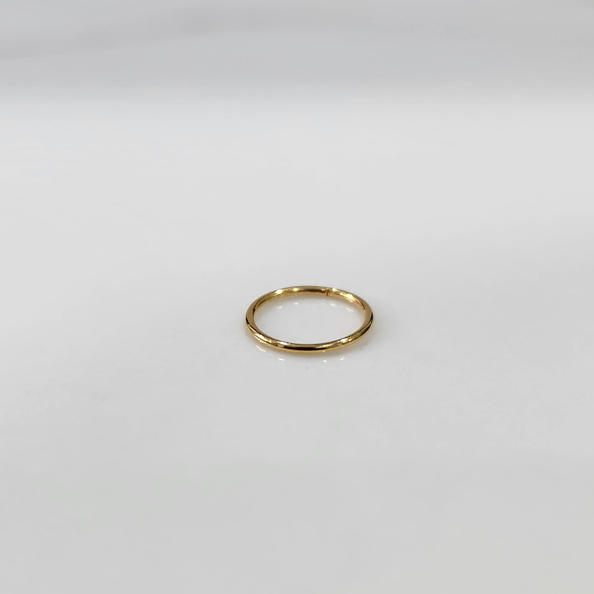 Flat lay view of small plain gold hoop nose ring on a light surface showing true size