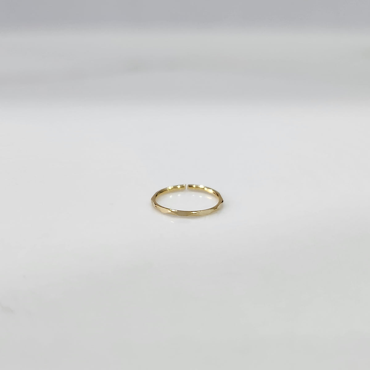 Top view of small plain gold hoop nose ring placed flat on a light grey surface to show actual size