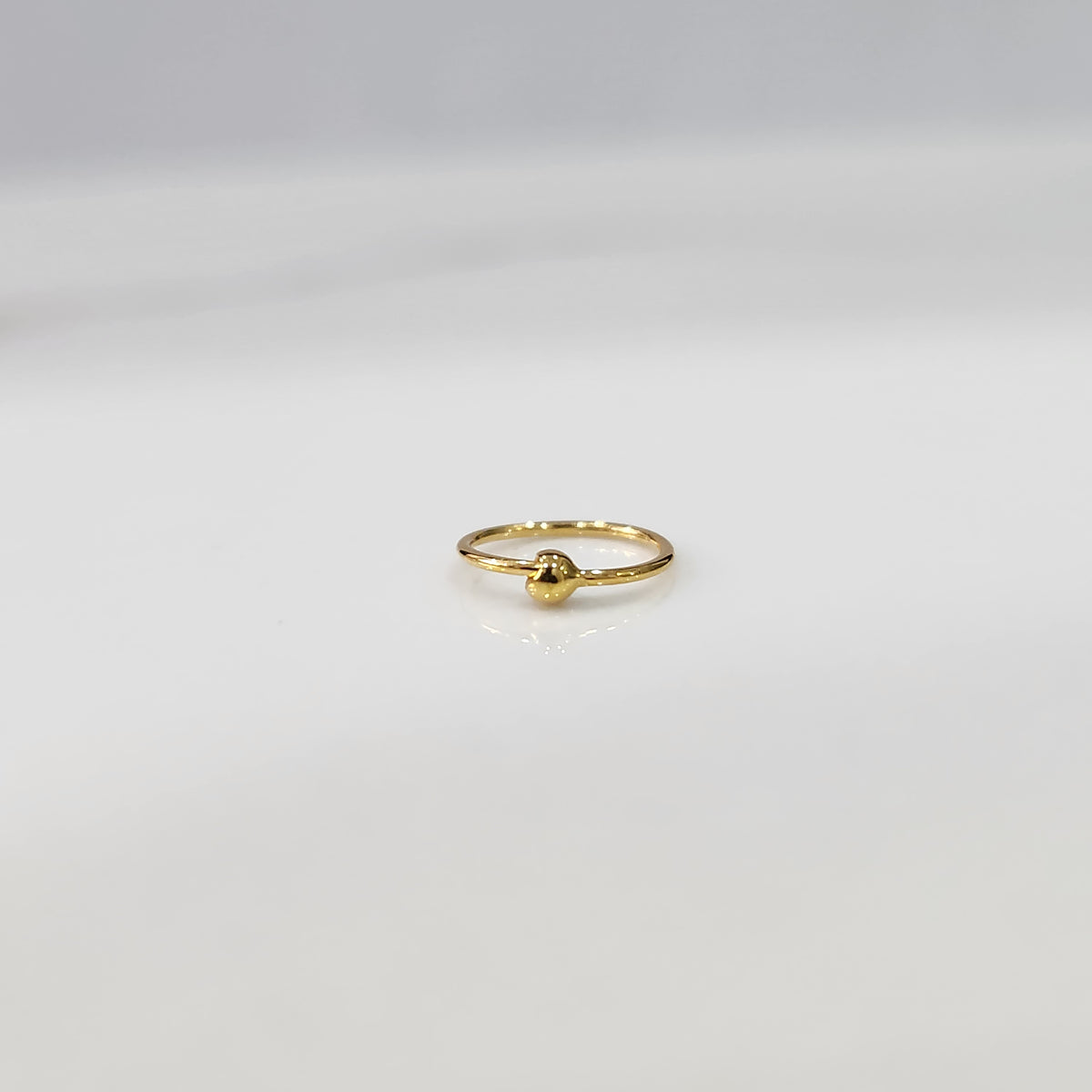 Flat lay view of small open hoop gold nose ring on a white surface showing its petite size