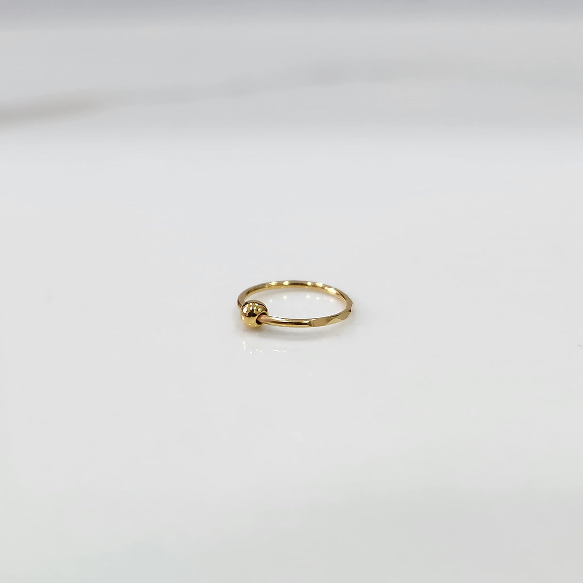 Flat lay view of petite open hoop gold nose ring on a white surface emphasizing its lightweight size
