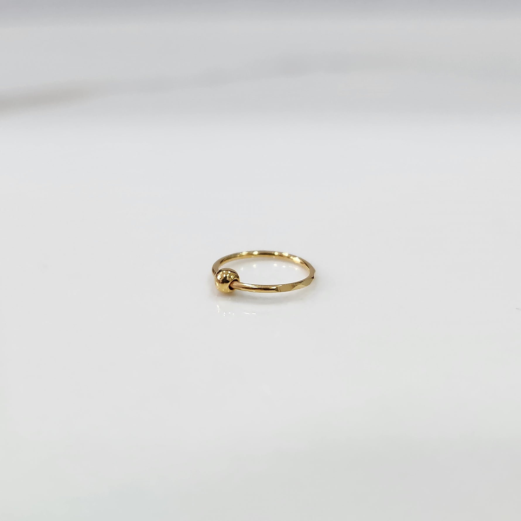 Flat lay view of petite open hoop gold nose ring on a white surface emphasizing its lightweight size