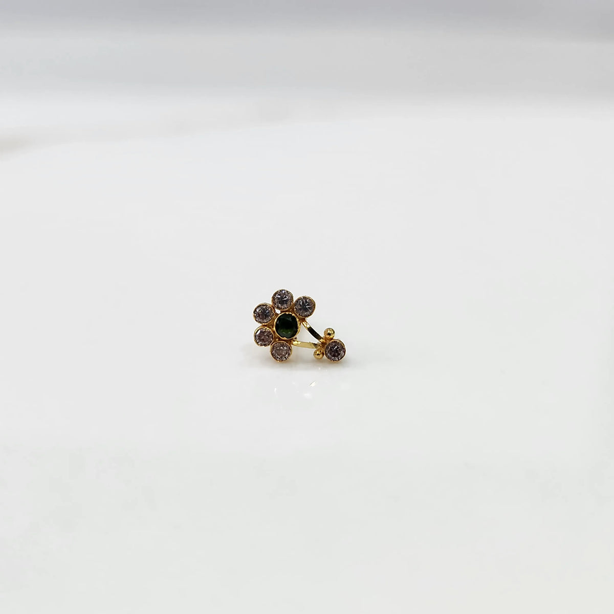 Front view of gold ring featuring clear floral gemstones with green center and drop pendant