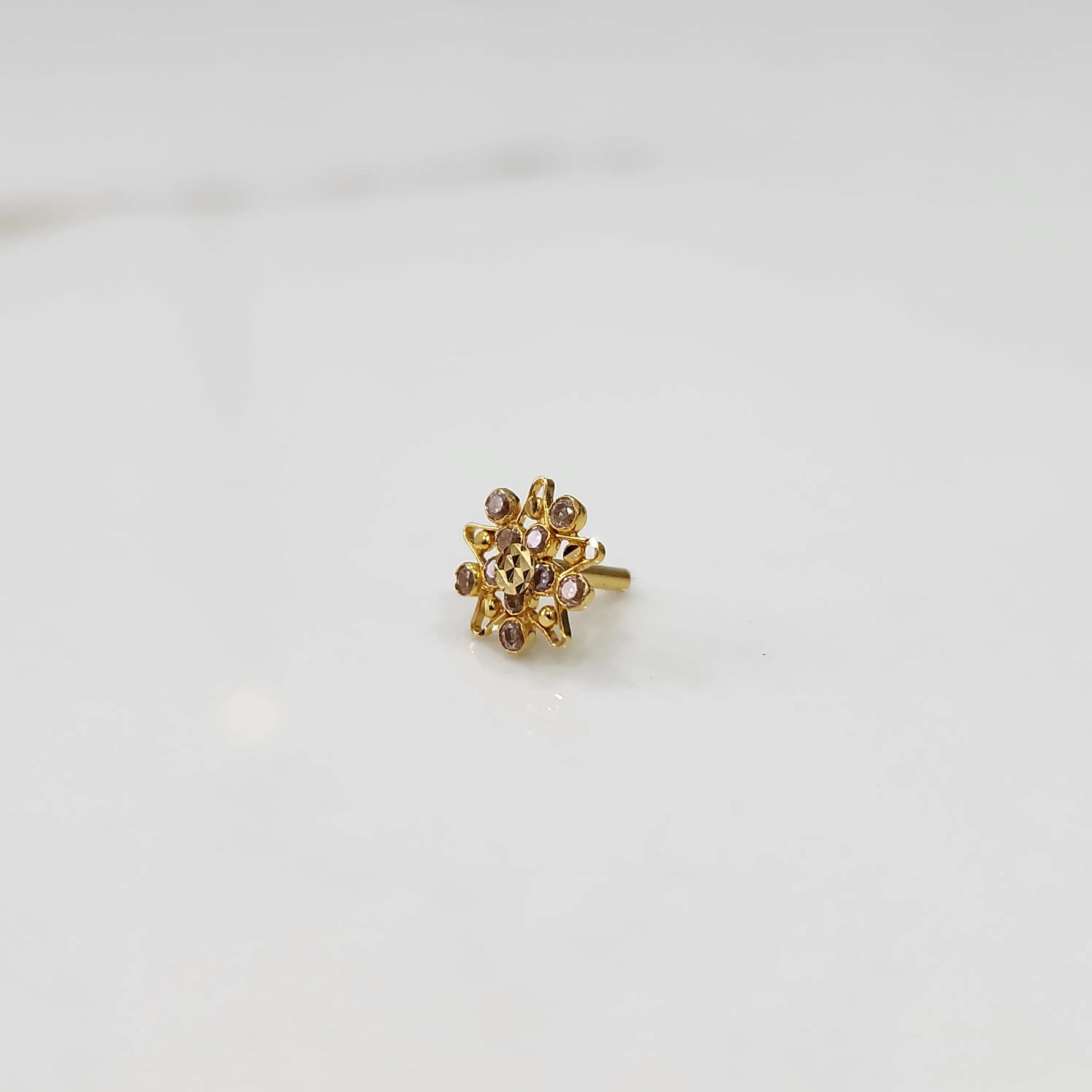 Side angle of handcrafted gold ring with flower motif and pink gemstones