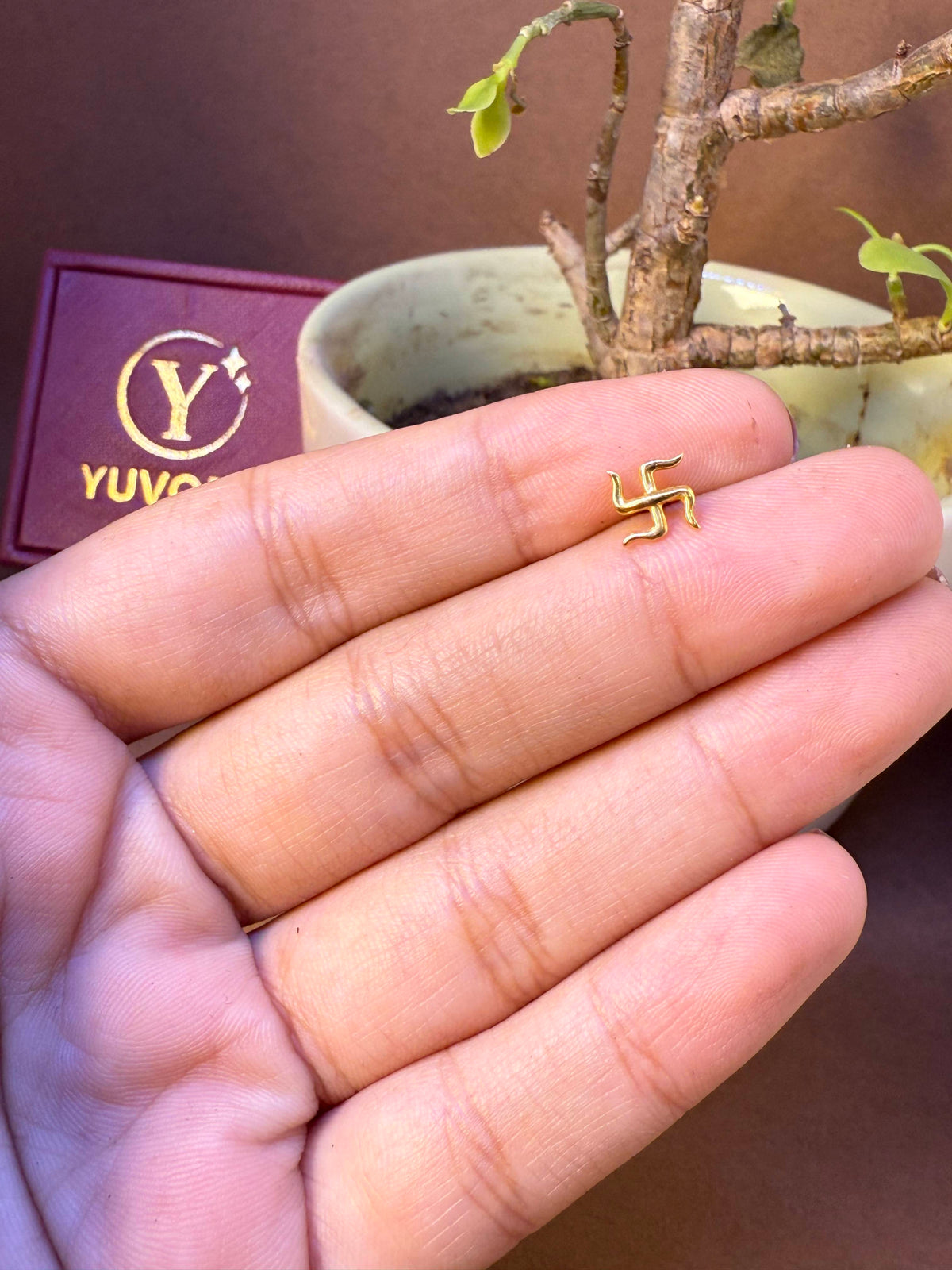 Gold nose pin featuring a traditional auspicious Hindu symbol, held in hand