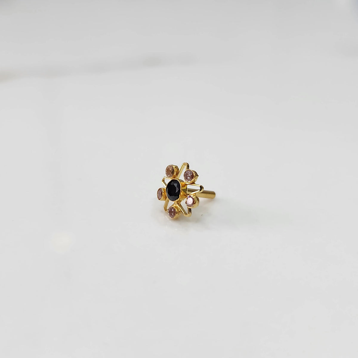 A gold nose pin shaped like a star with an oval black center stone and light pink and champagne accent stones