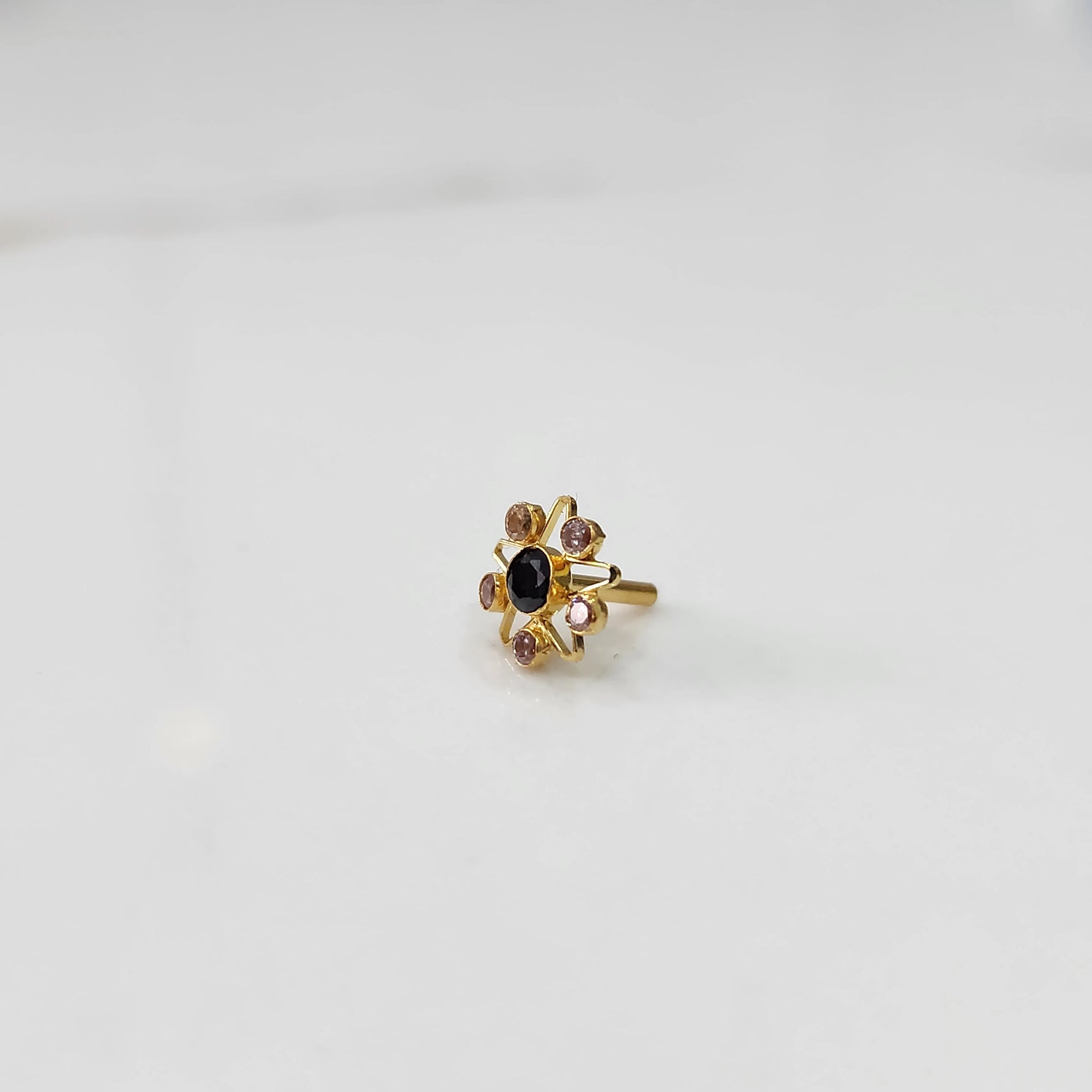 A gold nose pin shaped like a star with an oval black center stone and light pink and champagne accent stones